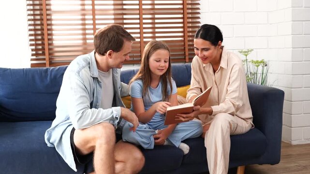 A warm and happy family is in the living room at home: father, mother, and their nine-year-old daughter sit on a couch. The father tells stories and sings songs with his daughter, while the mother hol