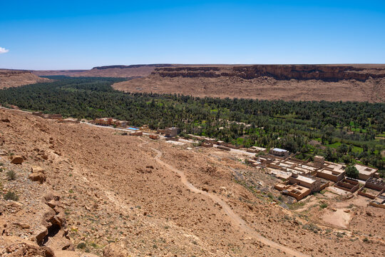 Draa Valley, high angle view of the lush green palm oasis of the Ziz Valley nestled between arid rocky cliffs with a traditional village in the High Atlas region of Morocco