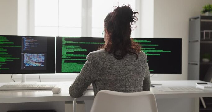 Developer programmer woman coding at computer workstation. Focused engineer and coder reviews software on triple screens in a bright office. Concept shows technology, productivity and focus.