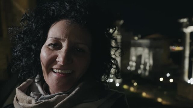 Stylish business woman smiling taking selfie with Temple of Saturn in Roman forum at background, while traveling in Rome at night