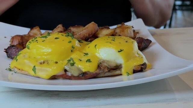 eggs benedict with hollandaise sauce being cut with knife