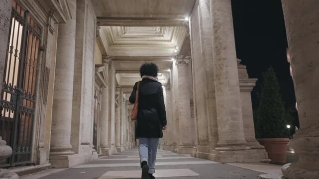 Stylish business woman walk on passage columns at Direzione museum at Capitoline in Rome, Italy at night, slow motion