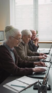 Vertical shot of group of seniors sitting in row and using laptops in computer class at retirement home, story format