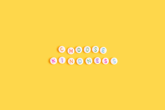 Choose kindness. Quote made of white round beads with multicolored letters on a yellow background.