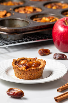 A mini apple pie tart on a plate with more in a muffin tin in behind.