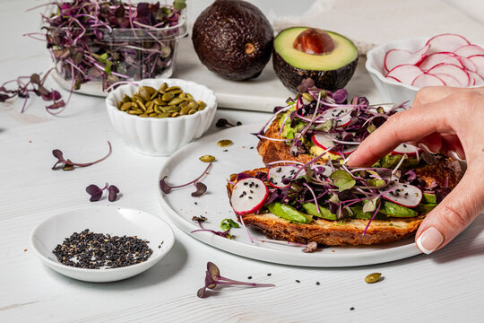 A hand reaching in to grab a slice of avocado toast with ingredients all around.