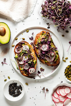 A plate of avocado toast topped with purple radish microgreens, ready for eating