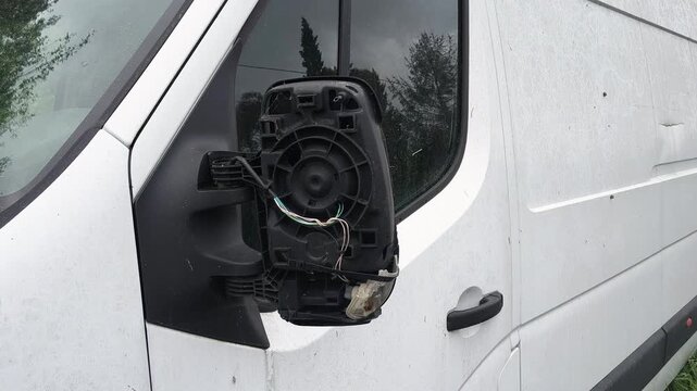 Broken car side mirror with exposed wires on white vehicle, close up damage detail, transportation accident concept, repair needed, safety risk, vandalism or collision aftermath.