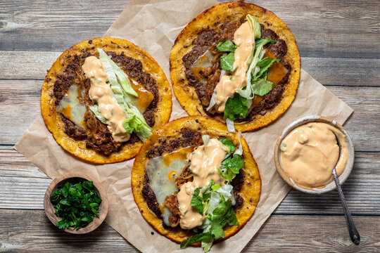 Smash burger tacos with burger sauce, lettuce, and parsley on the side.
