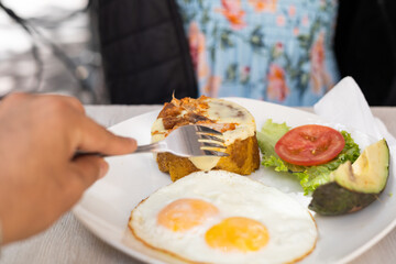 Young woman enjoying a traditional breakfast with green plantain eggs avocado and fresh tomato salad indoors. © Alejandro