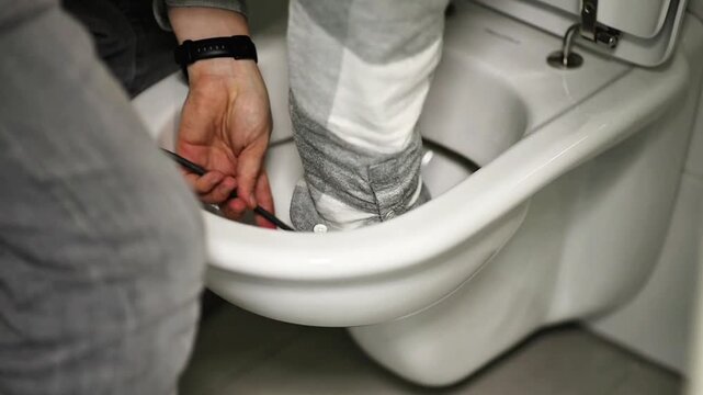 Plumber&rsquo;s hands in gloves using a clog remover cable to fix a blockage in a ceramic toilet bowl