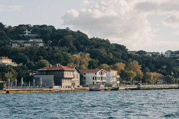 Obraz premium Panorámica de la costa de Estambul con residencias históricas y colinas verdes. Paisaje urbano junto al mar Bósforo en una tarde de navegación.