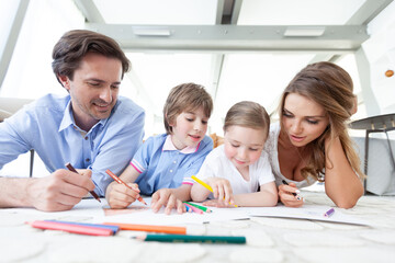 Fototapeta premium Happy family drawing together on the floor in a bright room
