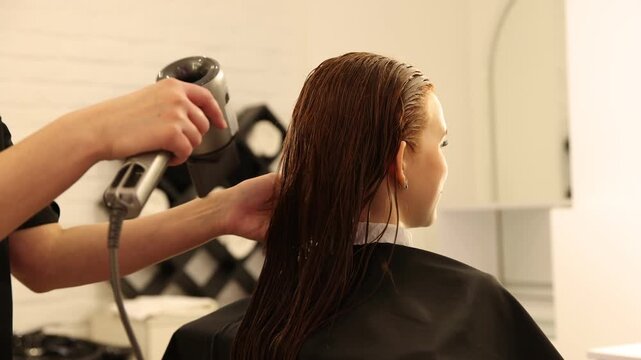 Stylist blow drying girl's hair in beauty salon, closeup