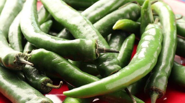 Fresh green chili peppers on red plate, closeup