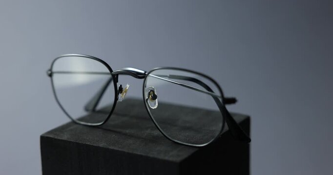Pair of stylish eyeglasses on podium against gray background, rotating