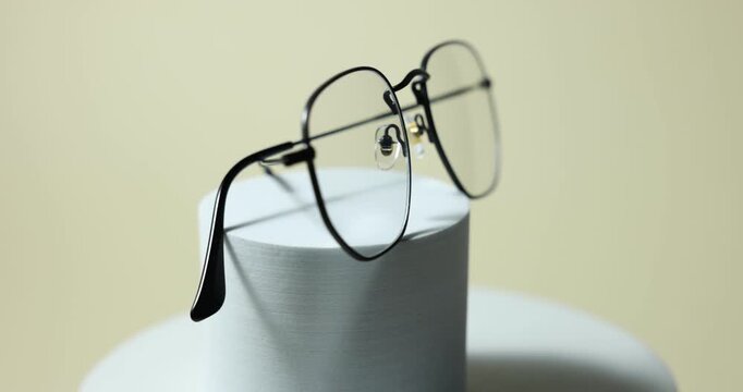 Pair of stylish eyeglasses on podium against light background, rotating