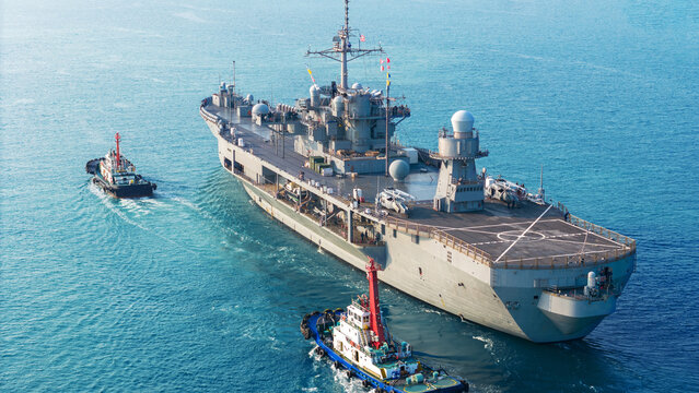 large naval amphibious assault ship being assisted by tugboats in the strategic Strait of Hormuz. Concept of maritime security, naval power projection, and protection of international shipping lanes.