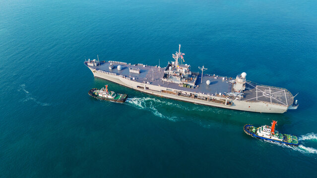 large naval amphibious assault ship being assisted by tugboats in the strategic Strait of Hormuz. Concept of maritime security, naval power projection, and protection of international shipping lanes.