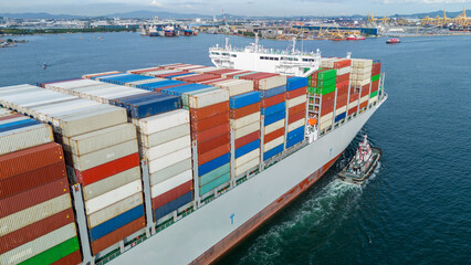 cargo container ship fully loaded arriving at the port. A small tugboat is pushing the huge vessel. Global maritime trade, freight transport, and logistics business concept. © Yellow Boat