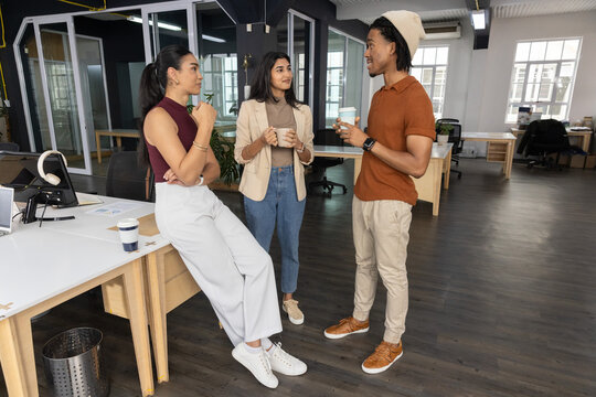 Vertical video: Chatting team holding mugs and cup in open office over coffee, in casual attire