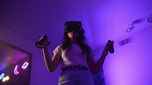 Young woman wearing VR headset confidently controlling virtual environment with controllers interacting with digital environment and mastering modern virtual reality technology
