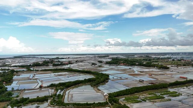 Expansive flooded farmlands from an aerial perspective, revealing intricate water patterns across a fertile landscape with distant settlements under a cloudy sky