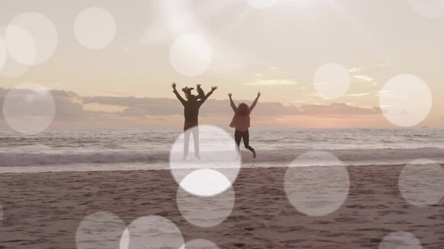 Couple nearing sand left raising arms, jumping marking sunset with bokeh hiding figures for design