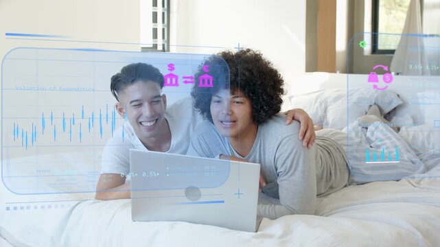 Two men lying on bed reviewing tech on laptop activating AR charts growing peaking receding smiling