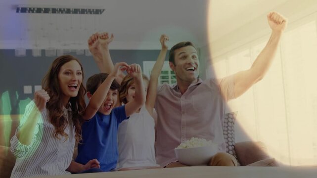Family raising arms and celebrating on couch after game cue, lens flares crossing faces, popcorn