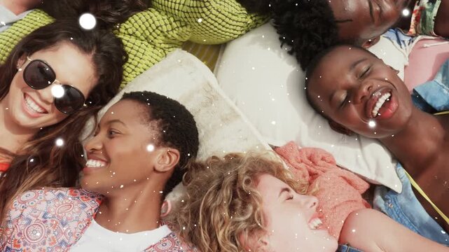 Camera panning seven friends lying heads on bed, sparkling over pillows, laughing for marketing
