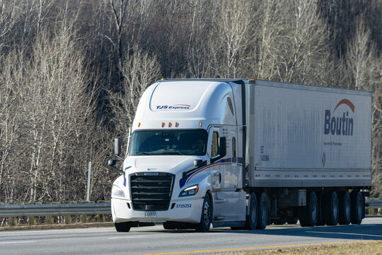 Quebec, Canada, 24 April 2026 : A white TJS Express Freightliner semi-truck with a Boutin trailer drives on a highway past bare trees.
