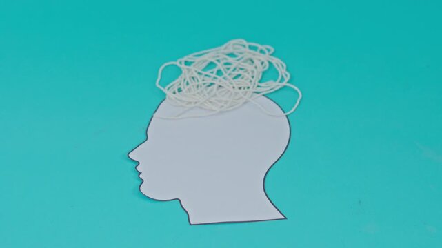 Paper cutout profile of human head with tangled white string on top symbolizing mental clutter or complex thoughts on turquoise background