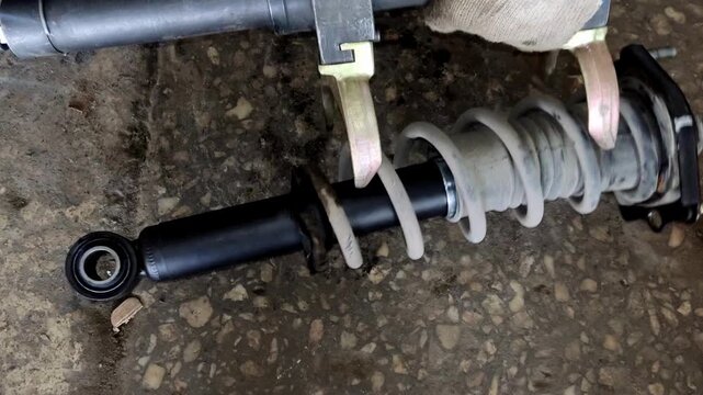 Gloved hand holding a car shock absorber with compressed spring