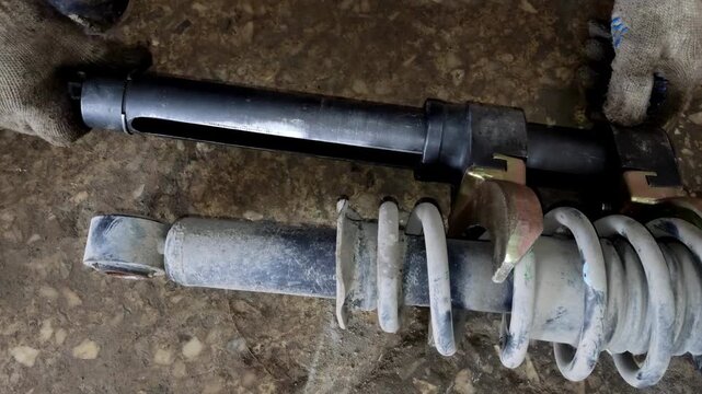 Gloved hand holding a car shock absorber with compressed spring