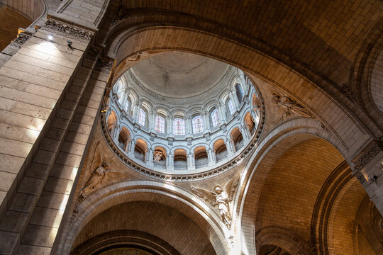 Multiple stone arches catch light and shadows under the interior dome of the Sacre Coer Basilica