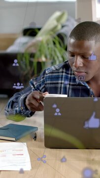 Vertical video: Man at laptop glancing down, reaching mug to sip while social media icons float
