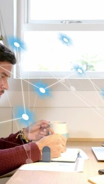 Vertical video: Man writing notes at desk, on lifting mug, blue nodes drifting over page for study