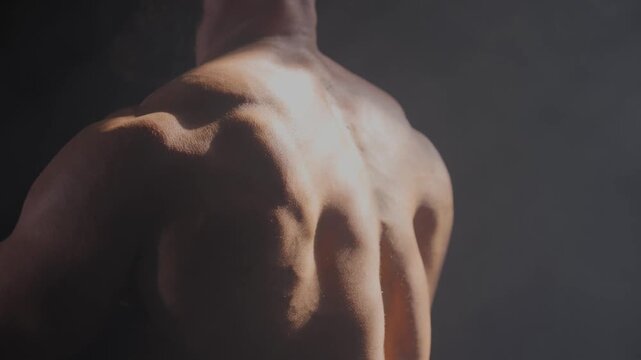 A male bodybuilder poses in shorts, showing off his back muscles.