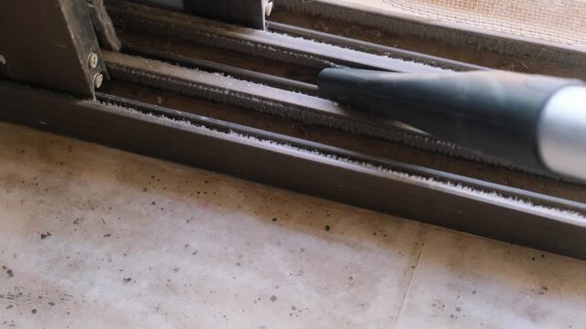 Detailed shot of removing dirt and debris from a window frame using a vacuum attachment