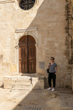 Detalle de turista mujer junto a la entrada de madera de la Iglesia de San Tito. Contraste de luces y sombras en la arquitectura hist&oacute;rica de piedra en Grecia.