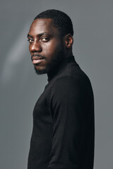 Obraz premium Portrait of African American man with dark skin wearing black turtleneck sweater in creative visual designer style. Studio shot with serious expression and side view on gray background.