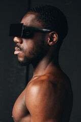 African man with dark skin and short hair wearing futuristic black sunglasses in creative conceptual visual style. Profile portrait with bare shoulders and modern fashion accessory. © SHOTPRIME STUDIO