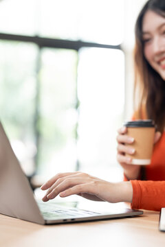 Close up of woman hands typing on laptop with coffee in cafe.