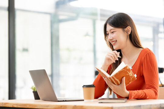 Enthusiastic Asian Woman Taking Notes While Working on Laptop in Cafe