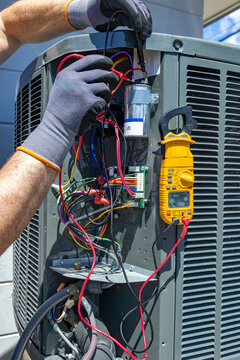 HVAC technician testing an outdoor AC unit capacitor with a multimeter, USA