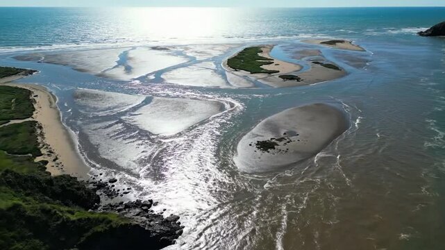 Waves of river and sea meet along the shore in a coastal location during daylight hours with clear skies and calm waters