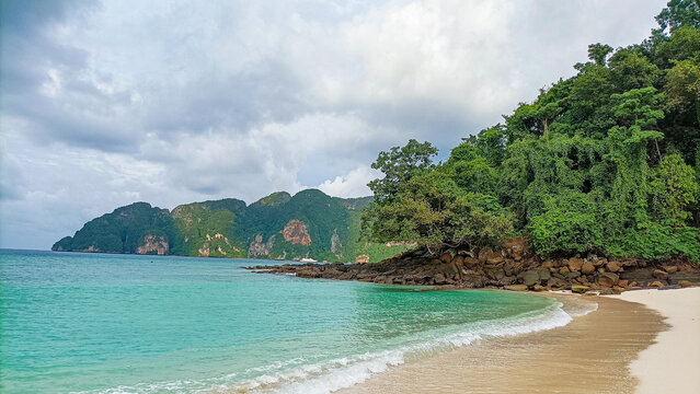 Phi Phi Island on August 15, 2025: Tropical beach shoreline with lush greenery under cloudy skies