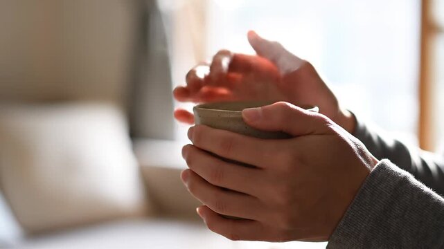 Person warming hands on a hot cup of steaming coffee in a cozy home