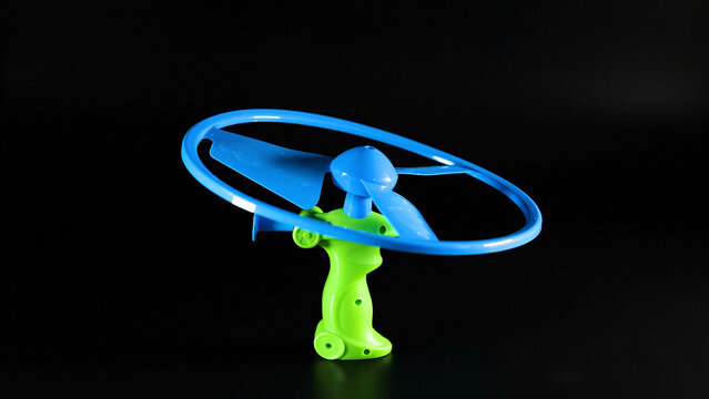 Blue and Green Plastic Pull String Flying Toy on Black Background